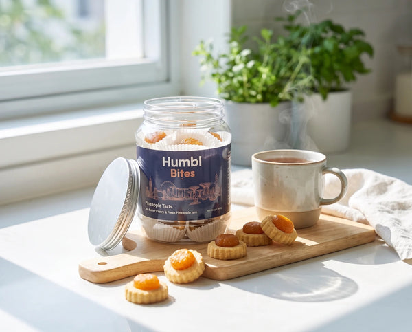 A jar of Humbl Bites pineapple tart sits on a wooden board next to a steaming mug in a bright kitchen setting.