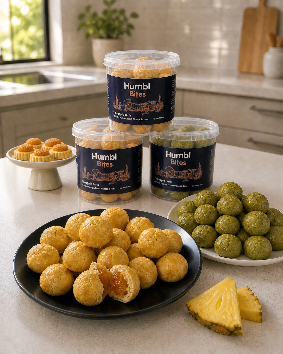 Three clear plastic tubs of Humbl Bites pineapple tarts on a kitchen counter, alongside plated golden ball of pineapple tarts, and pineapple wedges. The scene is set in a bright, modern kitchen with a sink and cabinets in the background.