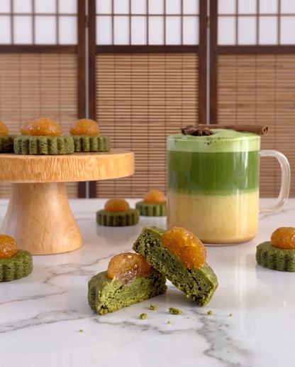 Matcha pineapple tarts, with a layered oat milk matcha latte, arranged on a marble surface with a wooden cake stand and shoji screen background.