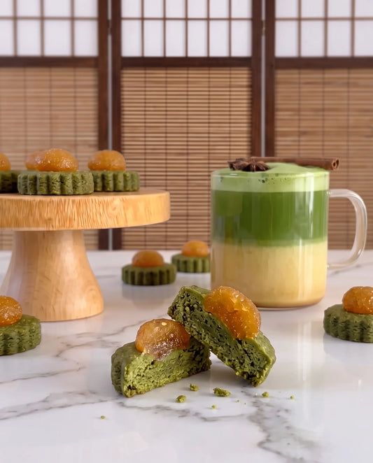 Matcha pineapple tarts, with a layered oat milk matcha latte, arranged on a marble surface with a wooden cake stand and shoji screen background.